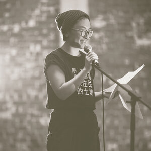 Person wearing glasses and beanie speaking into a mic